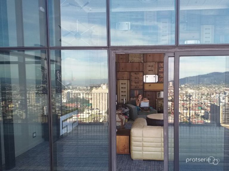 Fernanda Prats trabalhando em um espaço de coworking com vista para a cidade de San José e montanhas.